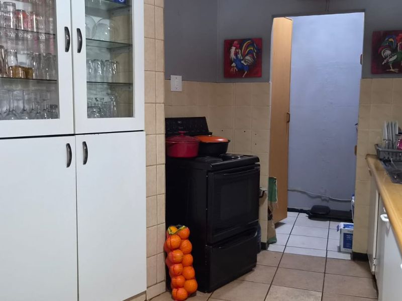 A functional kitchen featuring built-in cabinetry, a tiled backsplash, a freestanding stove, and a double sink with tiled flooring.