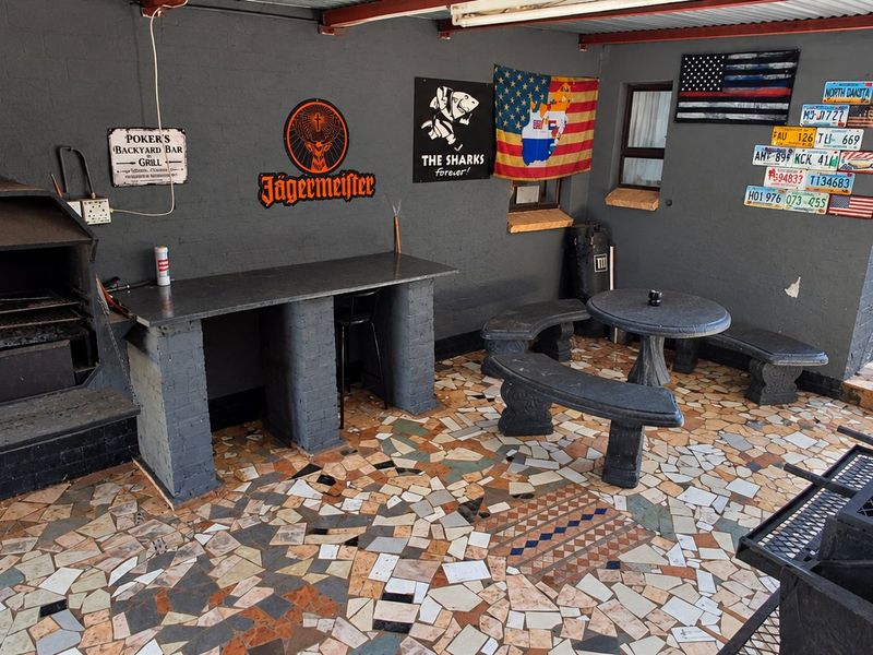 Covered outdoor patio area featuring a built-in braai, stone tile flooring, and fixed masonry seating, ideal for outdoor entertaining.