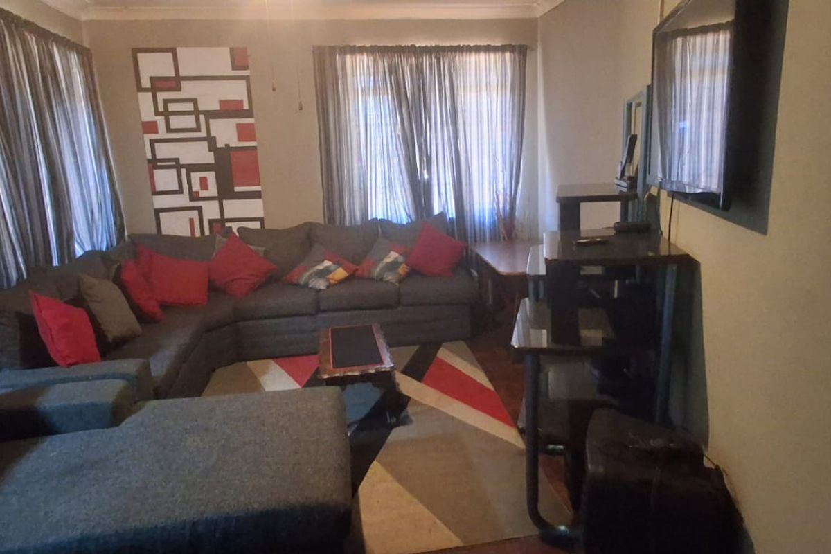 A living room featuring ceiling fan and decorative cornicing, currently showing signs of wear including peeling paint on the wall.
