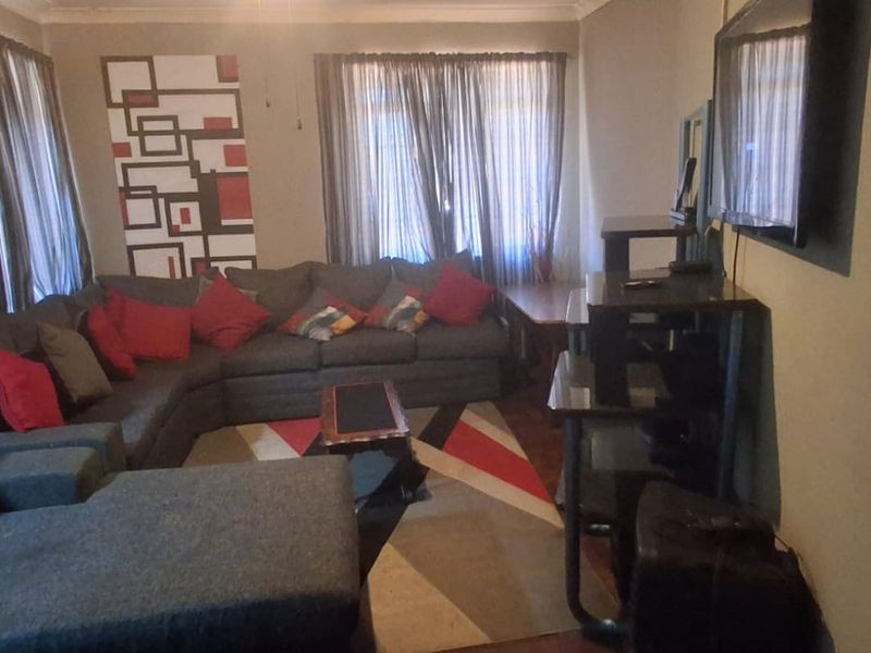 A living room featuring ceiling fan and decorative cornicing, currently showing signs of wear including peeling paint on the wall.