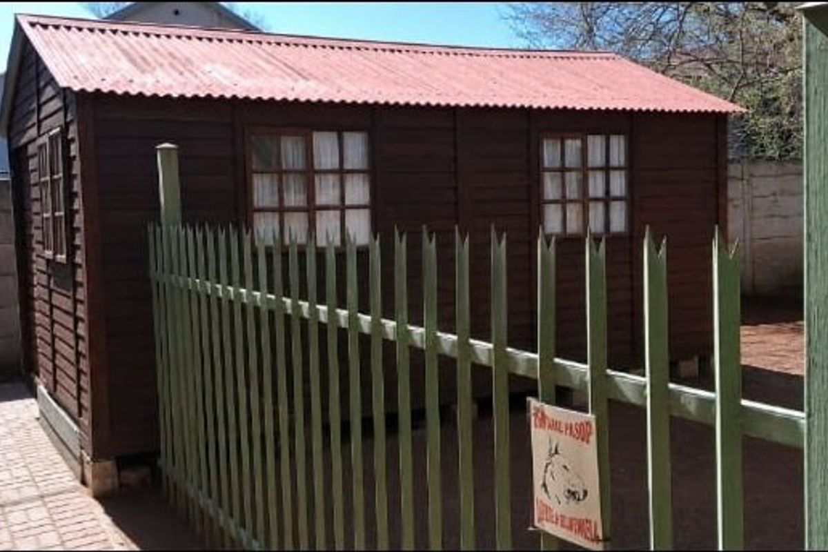 A detached timber-clad outbuilding with a corrugated metal roof, situated in a rear yard enclosed by precast concrete walls and a metal security fence.