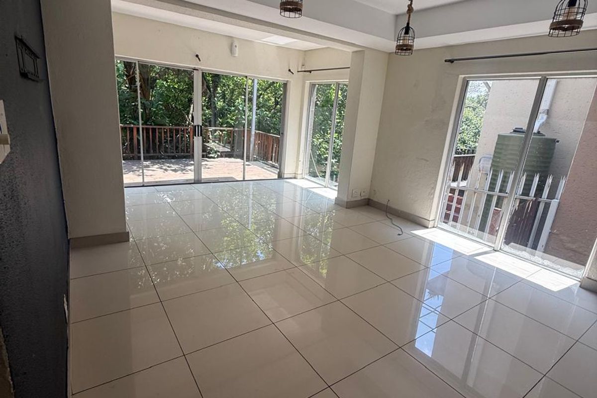 Spacious, empty living area featuring large format floor tiles, recessed ceiling details, and multiple sliding glass doors providing access to the outdoor deck.