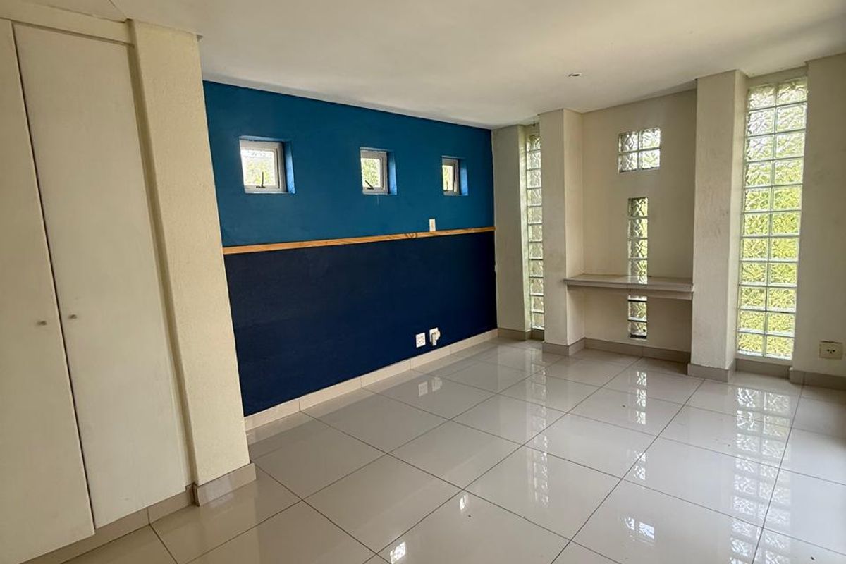 An empty bedroom featuring large format floor tiles, built-in cupboards, a built-in desk, and distinctive glass block windows providing natural light.