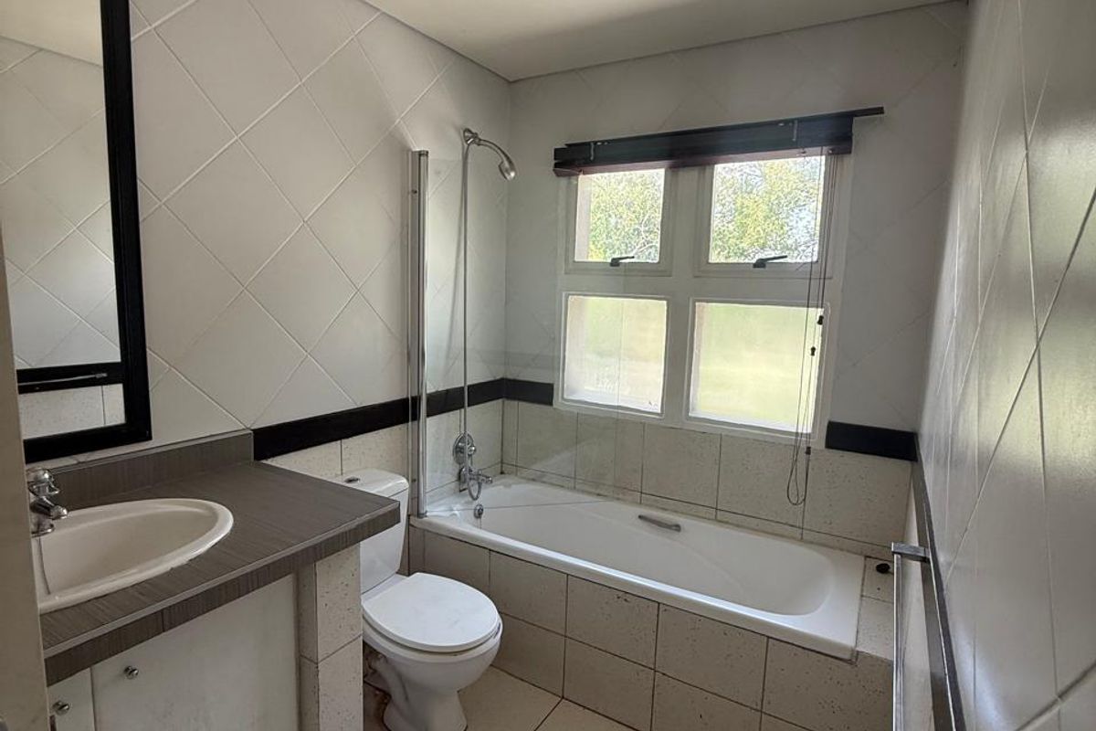 A functional bathroom featuring a built-in vanity, bathtub with shower mixer, glass screen, and tiled finishes throughout.