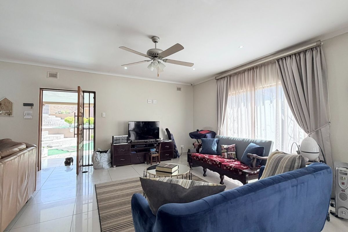 A bright and spacious living room featuring tiled flooring, a ceiling fan, and direct access to an outdoor patio area through a security gate.