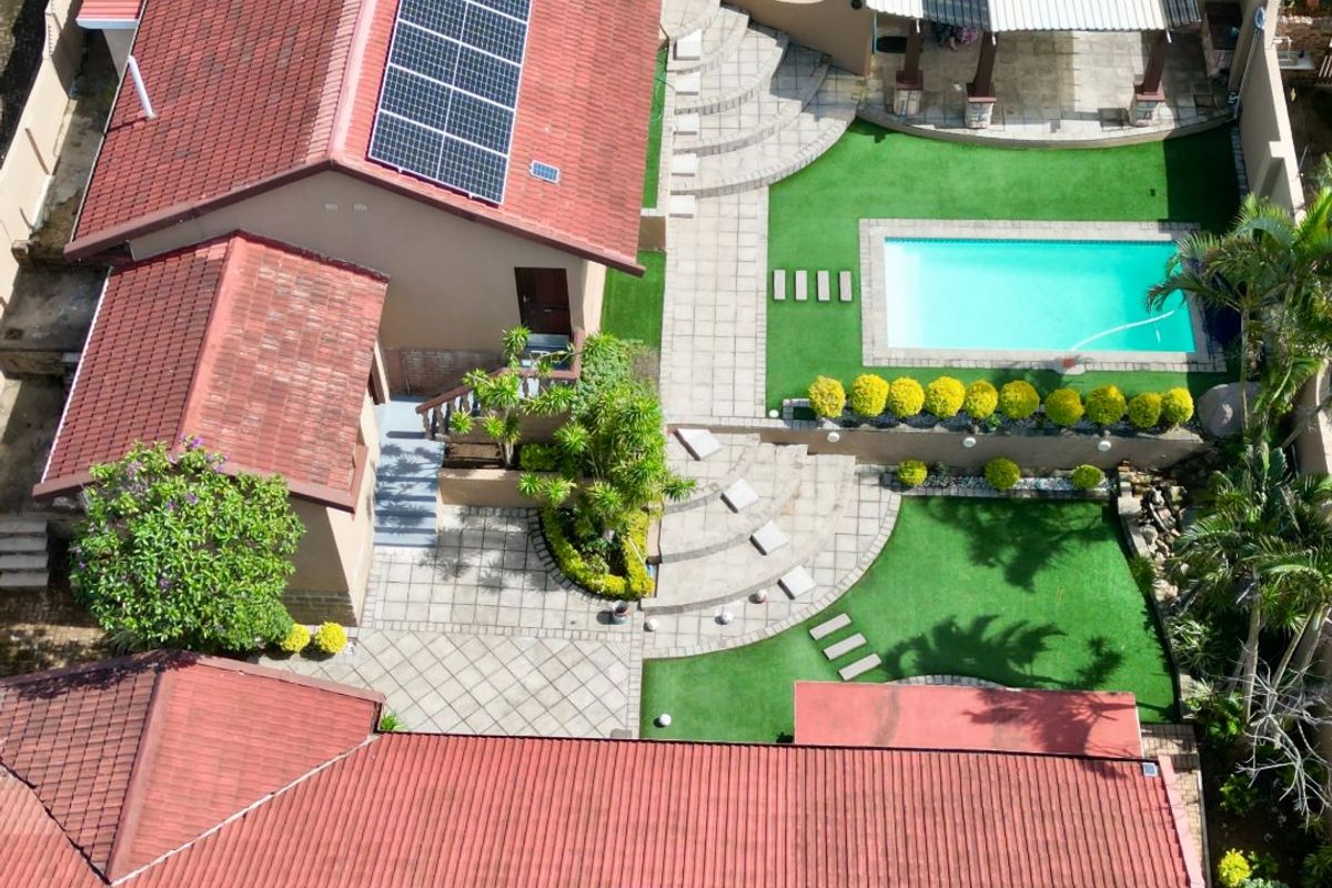 Aerial view of the property featuring a swimming pool, paved patio area with pergola, landscaped garden, and solar panels installed on the tiled roof.