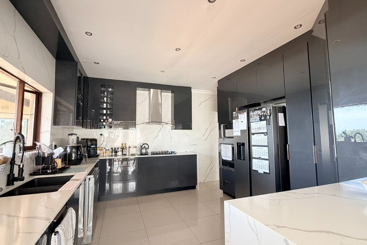 Modern kitchen featuring high-gloss cabinetry, stone countertops, marble-look splashbacks, and integrated appliances, offering a sleek and functional culinary space.
