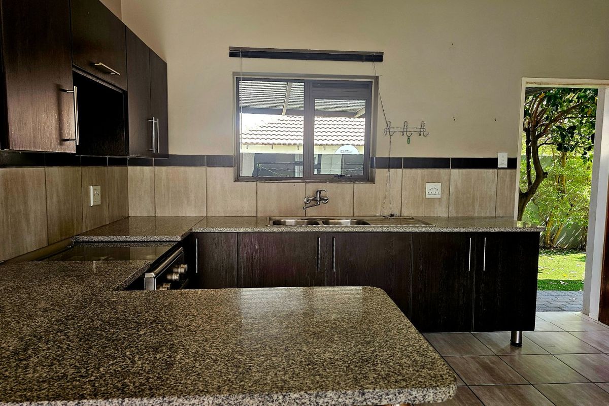 A functional kitchen featuring dark wood cabinetry, granite countertops, a double basin sink, and direct access to the garden area.