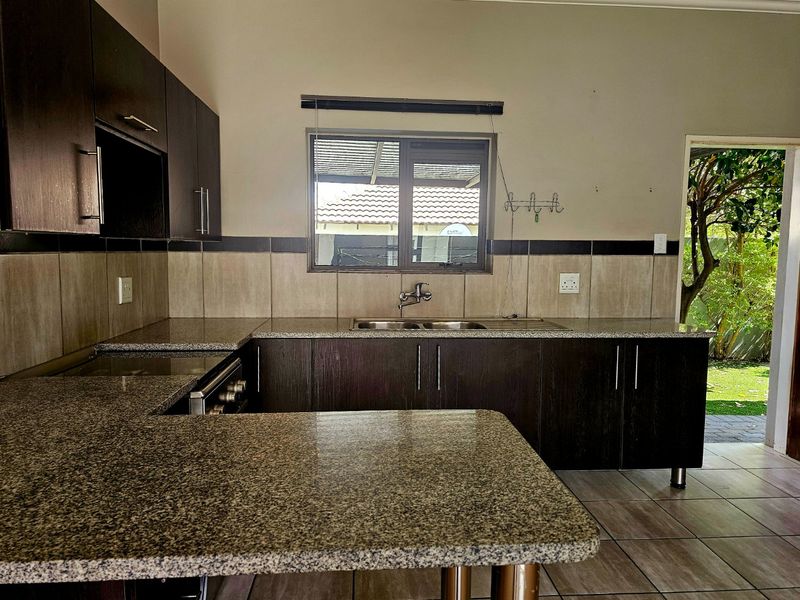 A functional kitchen featuring dark wood cabinetry, granite countertops, a double basin sink, and direct access to the garden area.