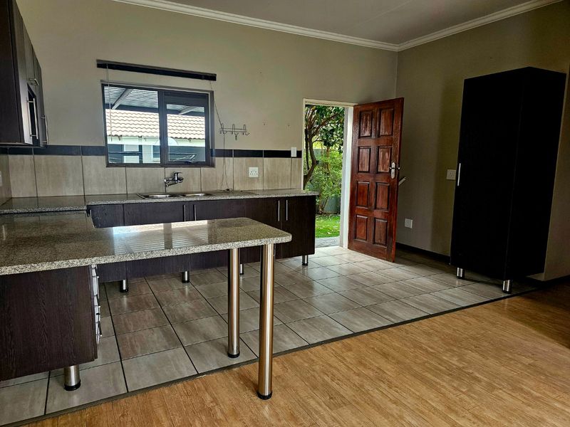 A functional kitchen featuring dark wood cabinetry, granite countertops, and a mix of tiled and laminate flooring with direct access to the garden.