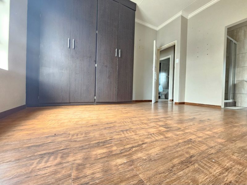 Spacious bedroom featuring dark wood-finish built-in cupboards, warm-toned laminate flooring, and direct access to an en-suite bathroom.