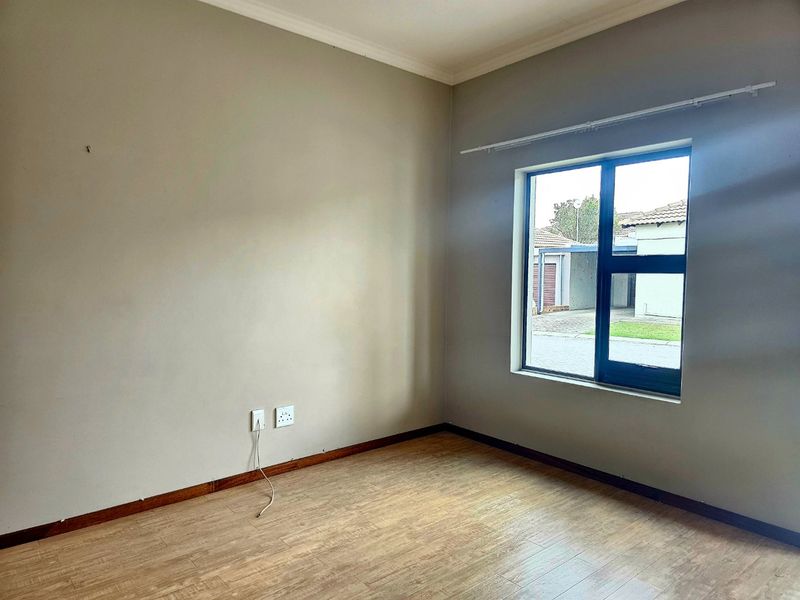 A vacant bedroom featuring neutral wall tones, durable laminate flooring, and a large aluminium-framed window providing natural light.