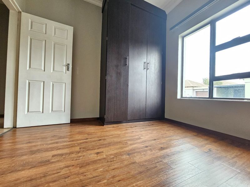 A bright, empty bedroom featuring modern laminate flooring, a dark wood built-in wardrobe, and a large window providing natural light.