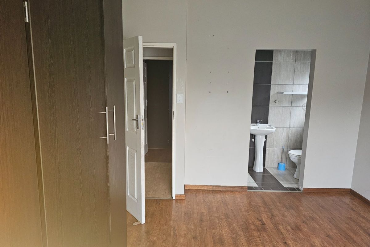 An empty bedroom featuring laminate flooring, a built-in wardrobe, and an open-plan en-suite bathroom with a pedestal basin and toilet.