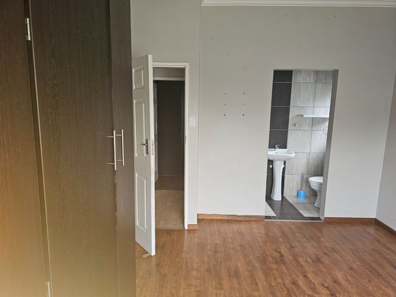 An empty bedroom featuring laminate flooring, a built-in wardrobe, and an open-plan en-suite bathroom with a pedestal basin and toilet.