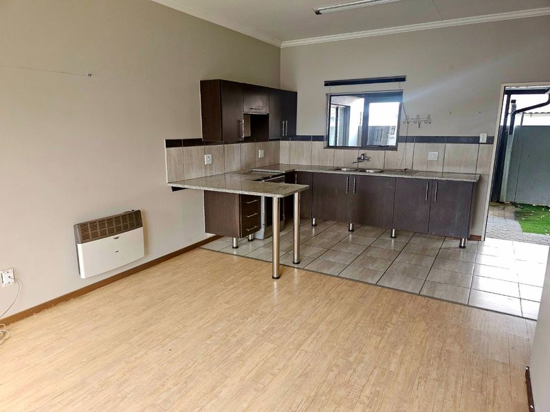 Open plan kitchen area featuring dark cabinetry, granite countertops, tiled backsplash, and a mix of laminate and tiled flooring with a wall-mounted heater.