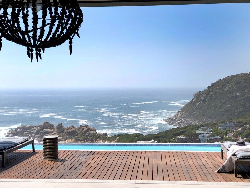 A stunning outdoor pool area featuring high-quality timber decking and an infinity-edge swimming pool overlooking a scenic coastal landscape.