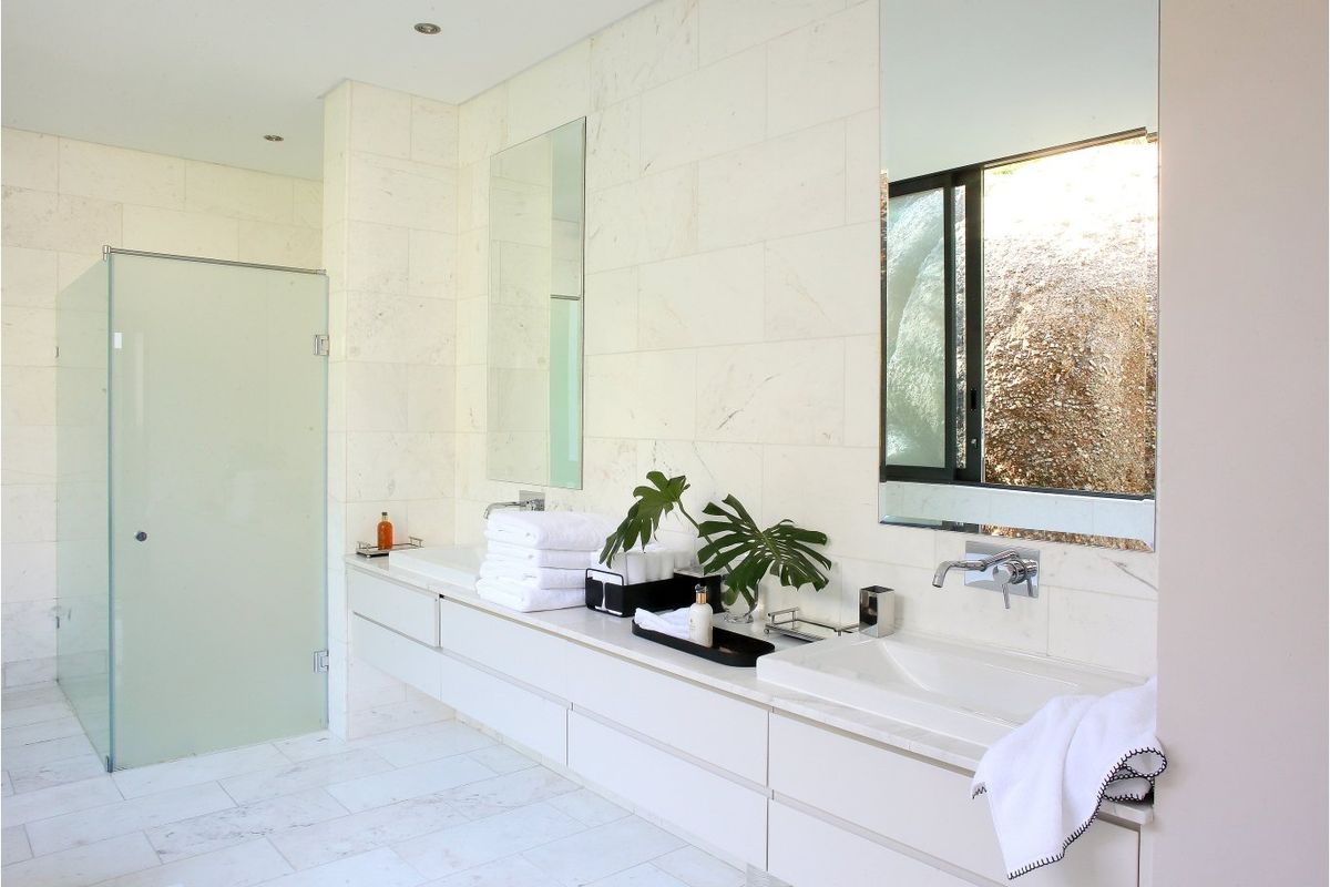 Modern bathroom featuring a sleek floating vanity with dual integrated sinks, wall-mounted faucets, stone tiling throughout, and a glass-enclosed shower.