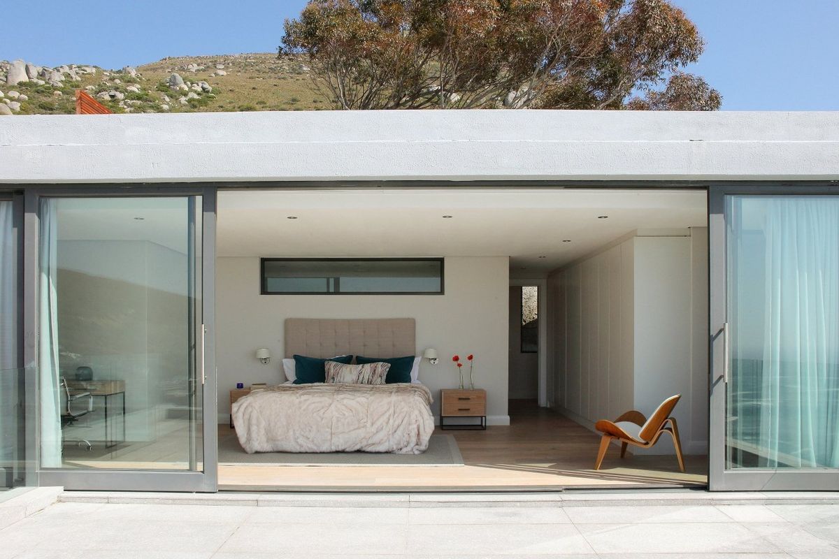 Modern bedroom featuring expansive sliding glass doors that open to an outdoor area, timber flooring, built-in cabinetry, and recessed lighting.