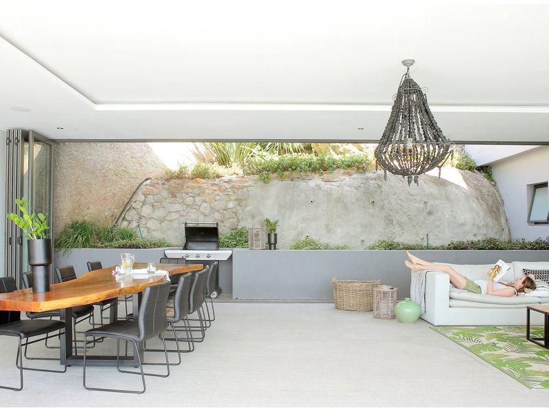 Spacious covered patio featuring a built-in braai, stone retaining wall, and seamless indoor-outdoor flow through large bi-fold doors.