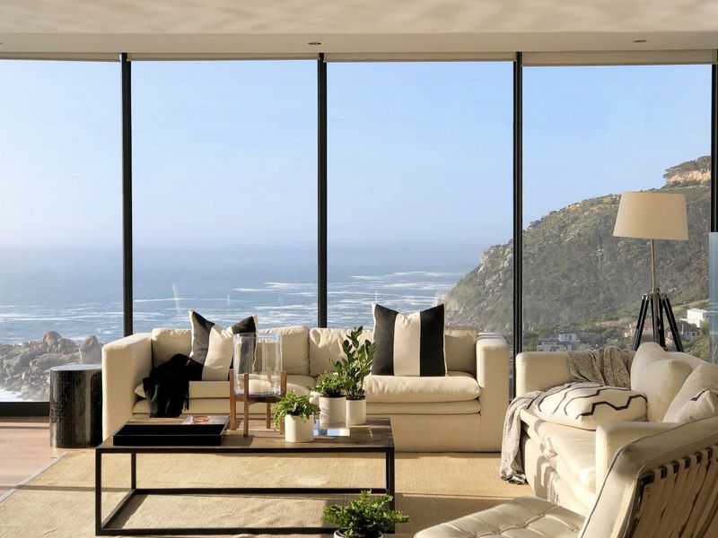 A bright, modern living room featuring expansive floor-to-ceiling windows that offer stunning, unobstructed ocean and coastal views.