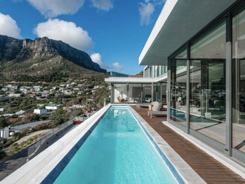 Modern lap pool with timber decking and expansive sliding glass doors, offering stunning mountain and coastal views.