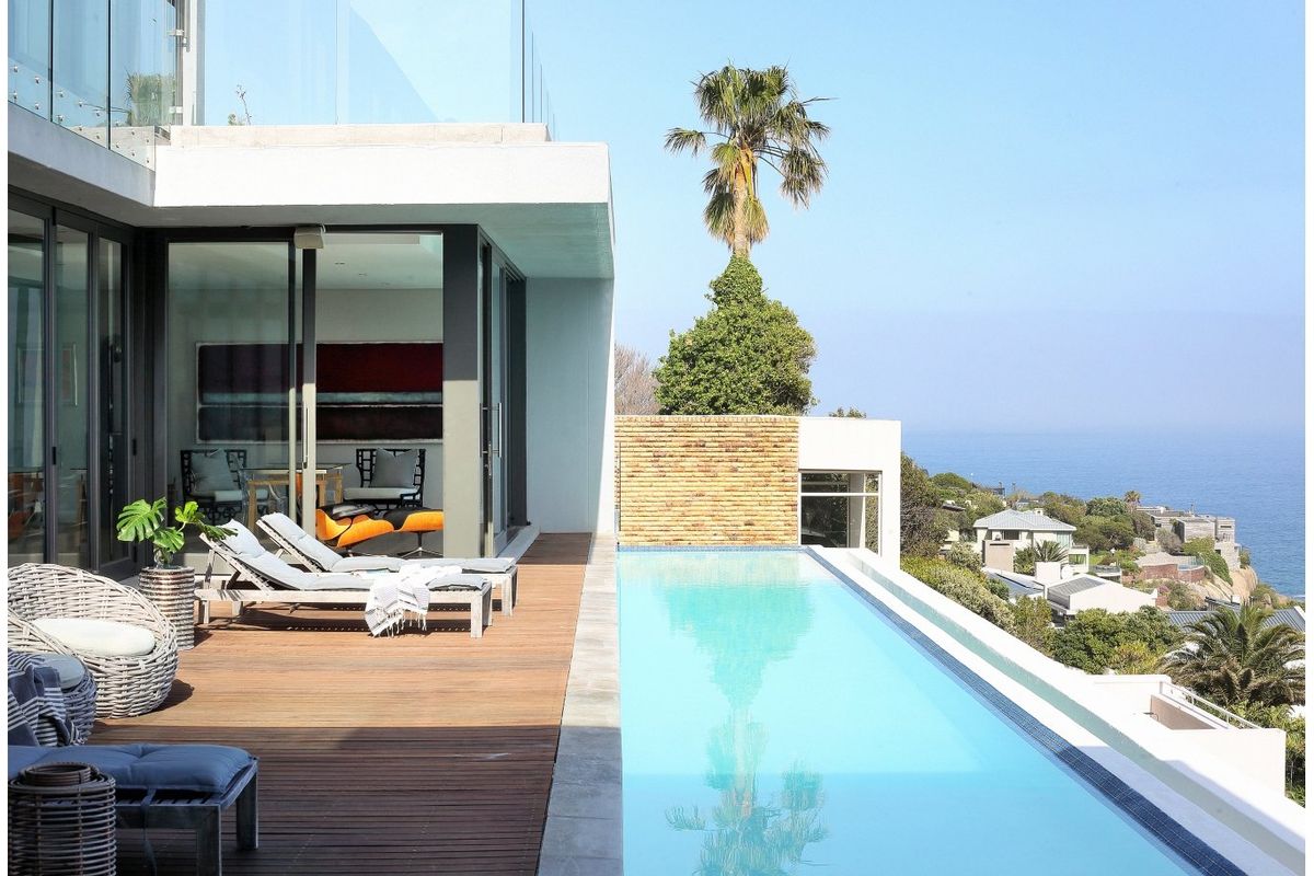 Modern outdoor living area featuring a sleek infinity edge swimming pool, timber decking, and glass balustrades with expansive coastal views.