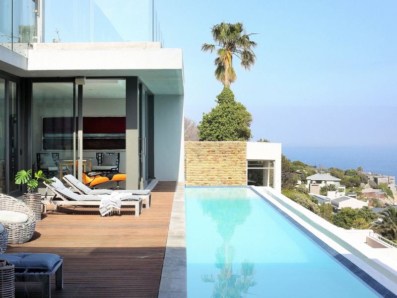 Modern outdoor living area featuring a sleek infinity edge swimming pool, timber decking, and glass balustrades with expansive coastal views.