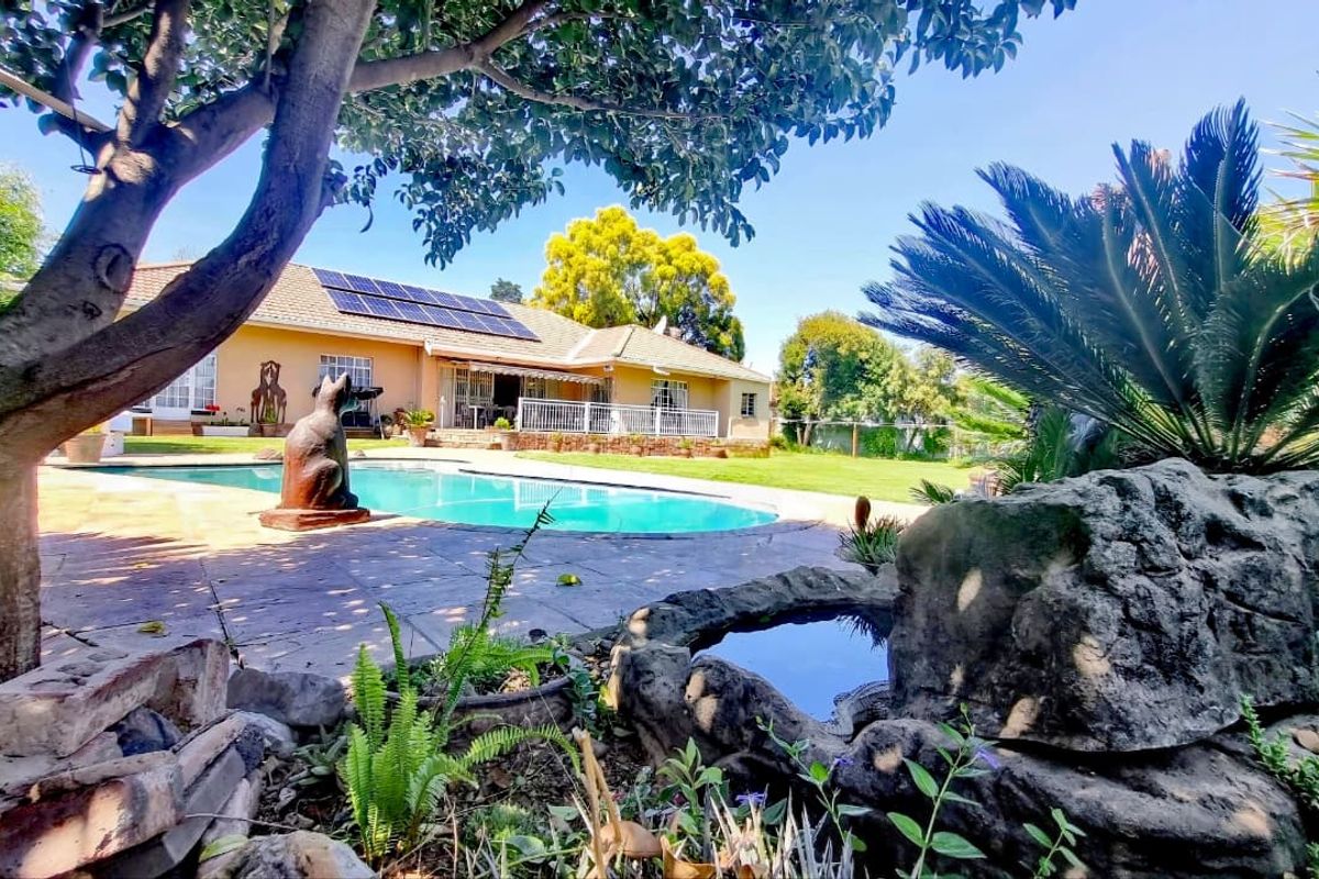 Spacious rear garden featuring a swimming pool, paved patio area, and solar panels installed on the roof of the main residence.