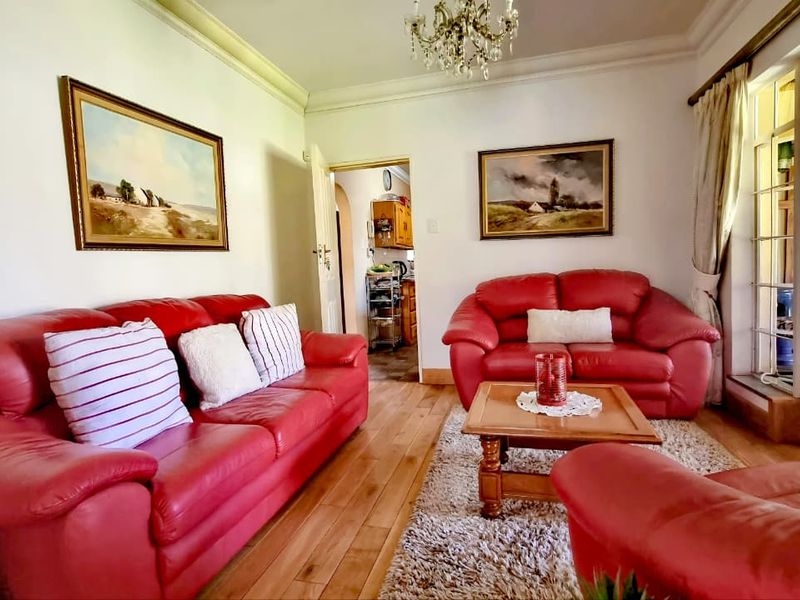 A cozy living room featuring hardwood flooring, crown molding, and a classic chandelier, with direct access to an adjacent room through French doors.