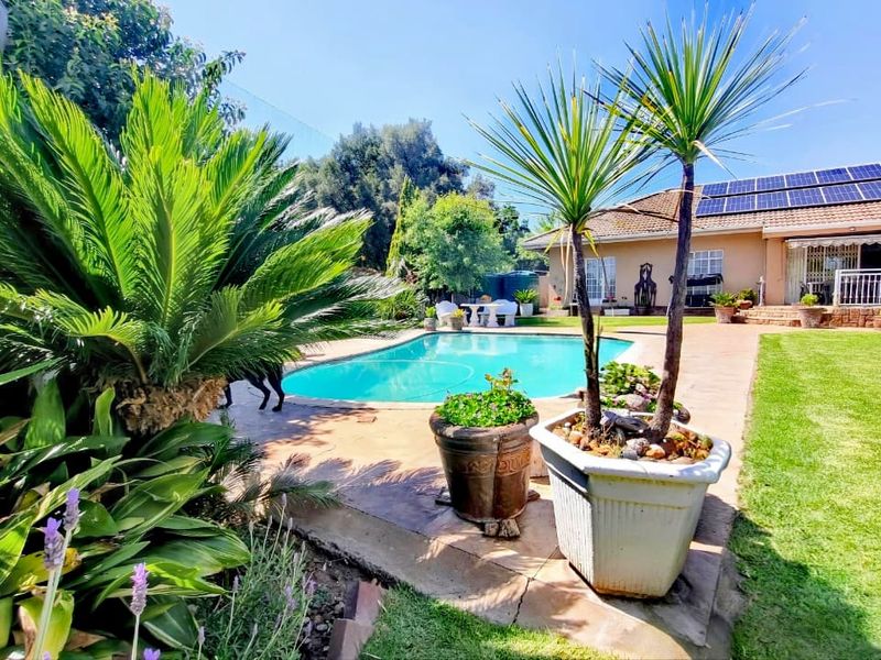 A well-maintained backyard featuring a swimming pool, paved patio area, and a house roof equipped with solar panels.