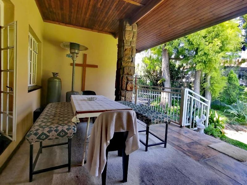 Covered outdoor patio featuring a stone-clad pillar, timber ceiling, and metal balustrade, overlooking a lush garden area.