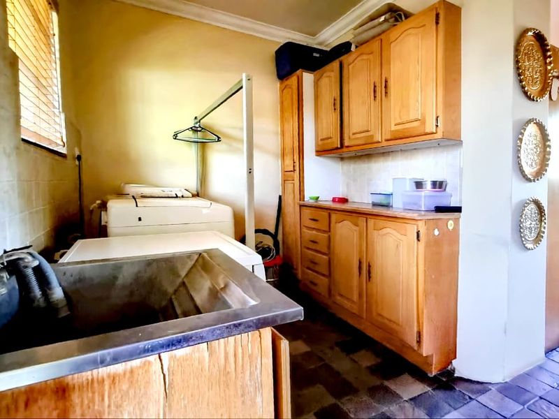 Functional laundry room featuring built-in wooden cabinetry, a stainless steel sink, and tiled flooring, offering practical utility space with potential for modernization.