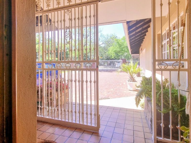 A covered patio area featuring tiled flooring and a security gate, leading out to a brick-paved outdoor space.
