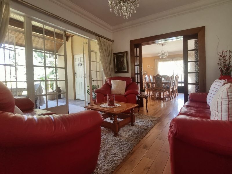Spacious living room featuring hardwood flooring, elegant crown molding, and large french doors providing access to the patio, with an adjoining dining area.
