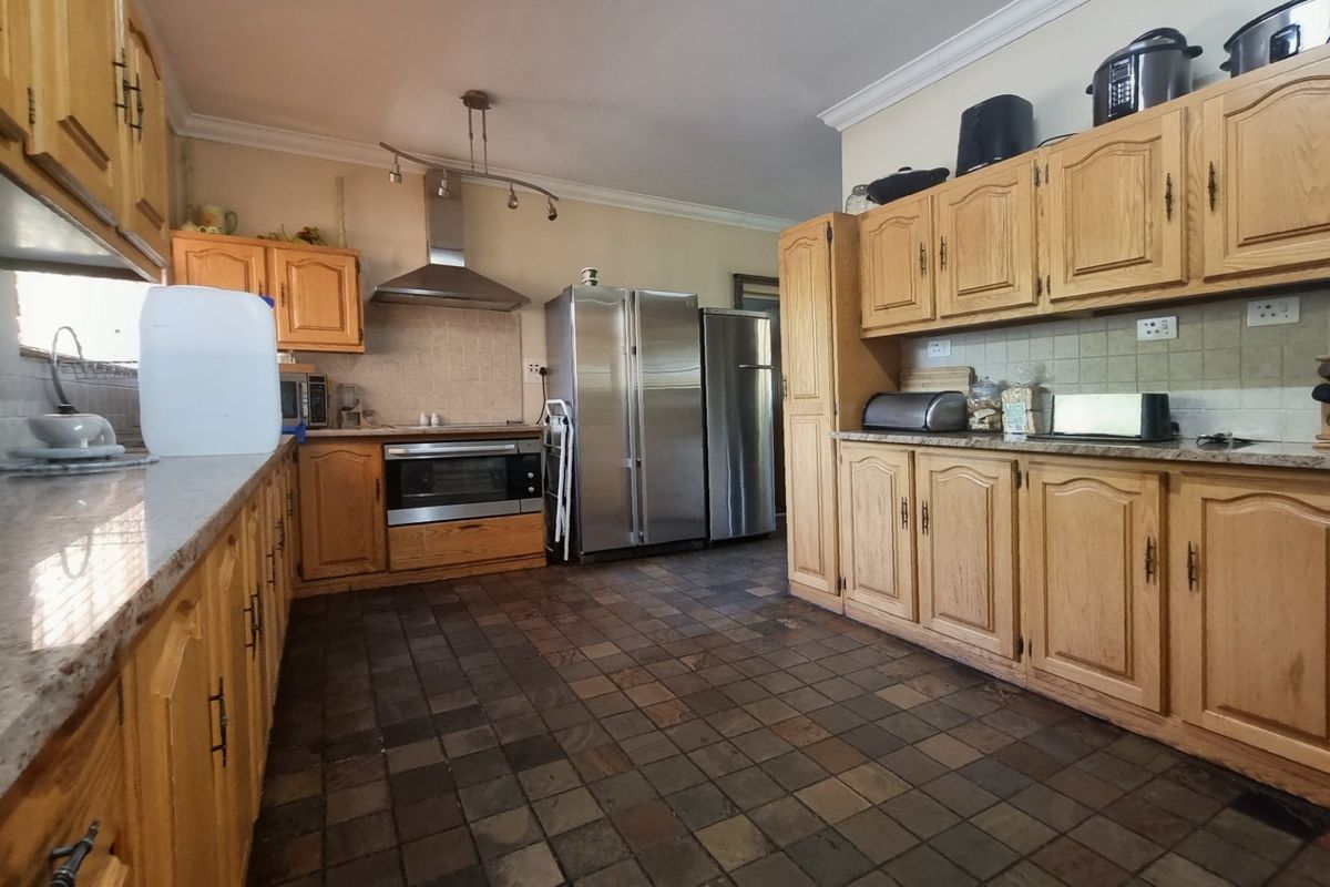 A spacious kitchen featuring traditional wooden cabinetry, granite countertops, tiled flooring, and built-in stainless steel appliances.