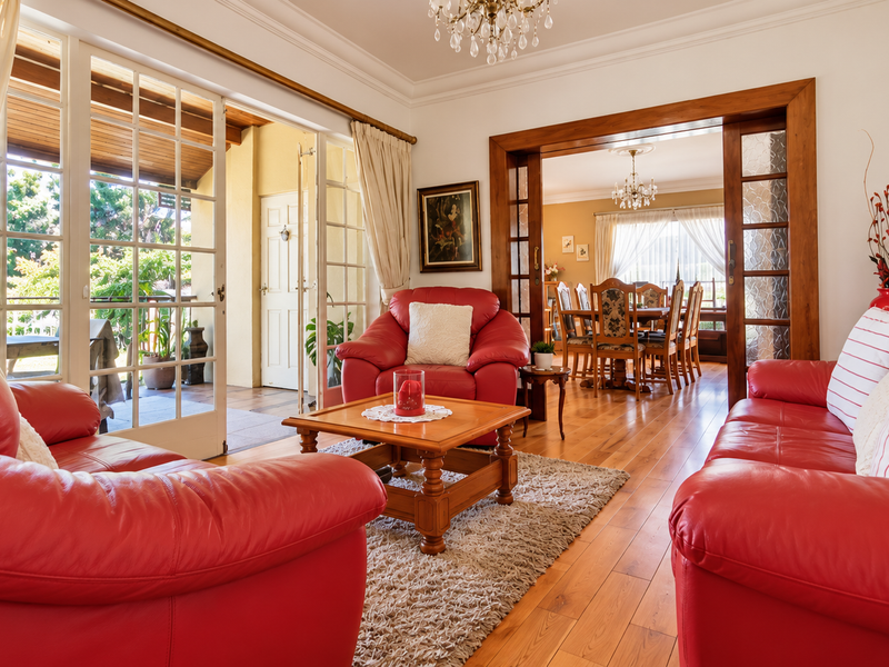 Spacious open-plan living and dining area featuring polished hardwood floors, elegant crown molding, and large french doors opening to a covered patio.