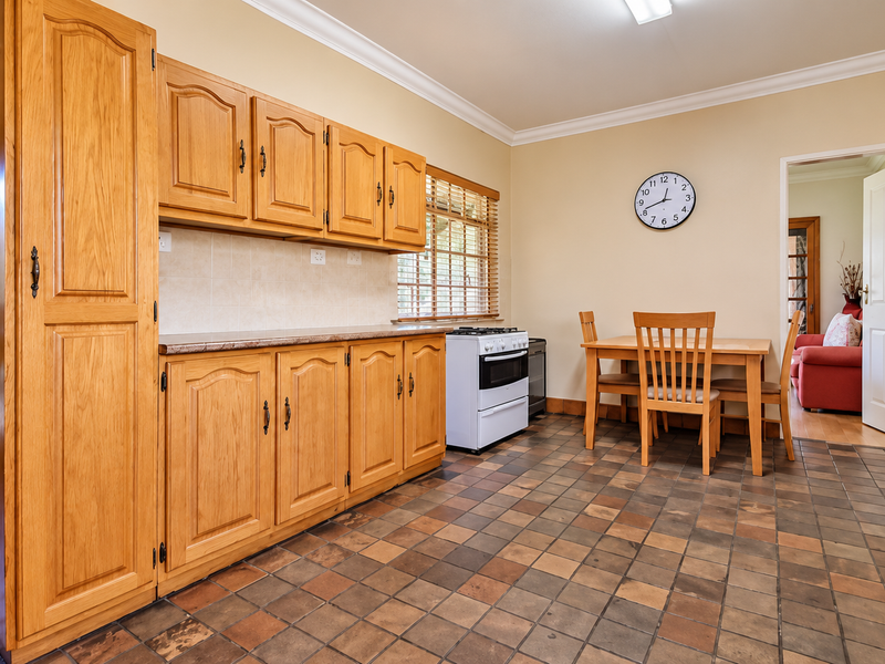 A functional kitchen featuring traditional oak cabinetry, laminate countertops, and durable tiled flooring, with an integrated dining area and direct access to adjacent rooms.