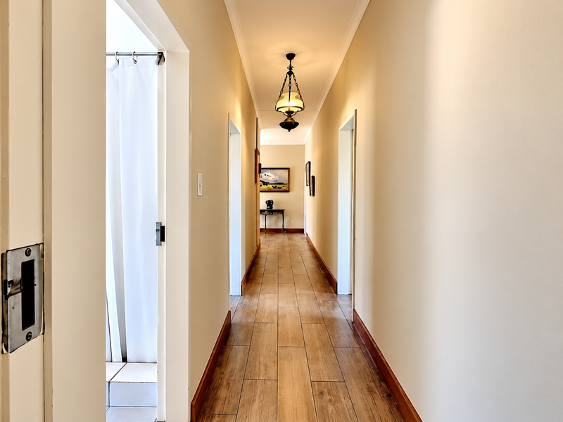 A clean, well-lit hallway featuring wood-look tile flooring, neutral walls, and classic pendant lighting, providing access to adjacent rooms.