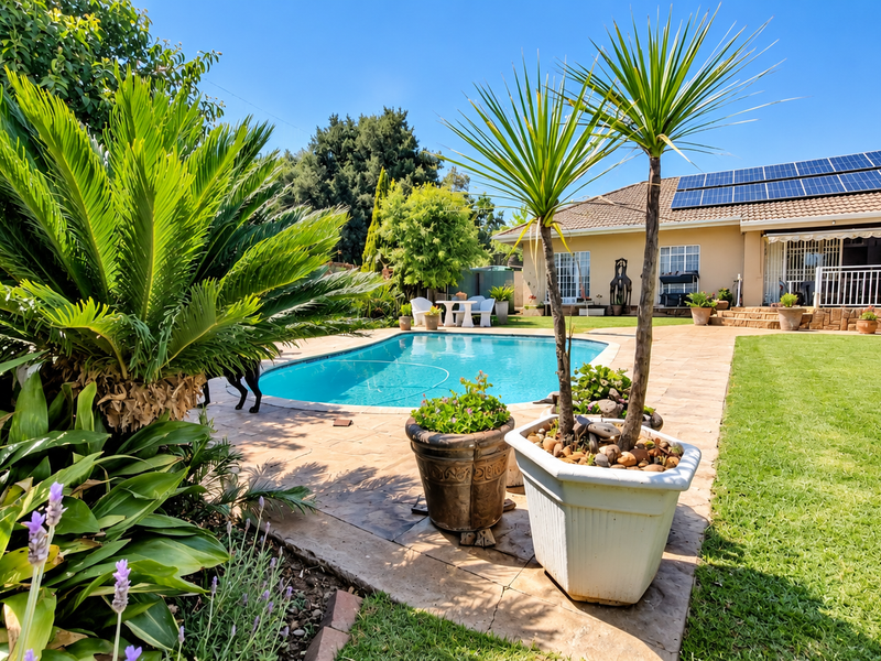 A well-maintained backyard featuring a swimming pool, paved patio area, lush lawn, and solar panels installed on the roof.