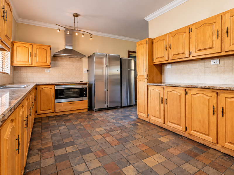 A spacious kitchen featuring traditional wooden cabinetry, granite countertops, slate tile flooring, and integrated stainless steel appliances, offering a functional and classic layout.