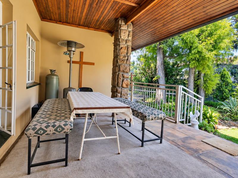 A covered patio featuring a timber ceiling, stone-clad pillar, and tiled flooring, offering direct access to the garden through classic french doors.