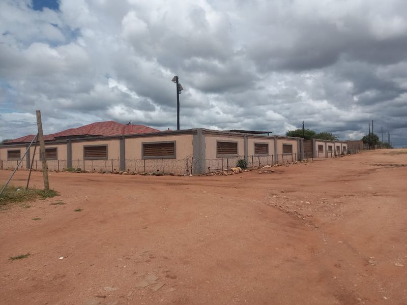 Exterior view of a property featuring a perimeter wall with security razor wire, tiled roof, and security shutters on windows.