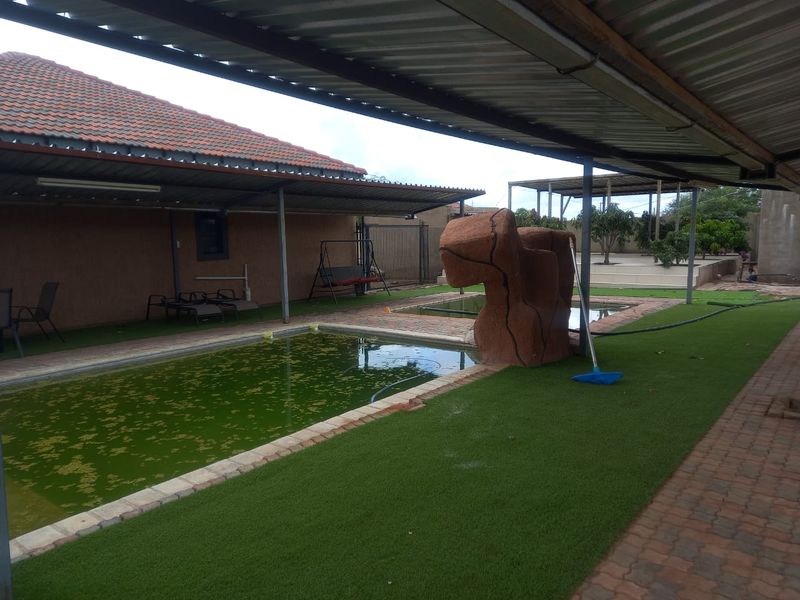 Outdoor pool area featuring a covered patio, artificial lawn, and a swimming pool requiring maintenance.