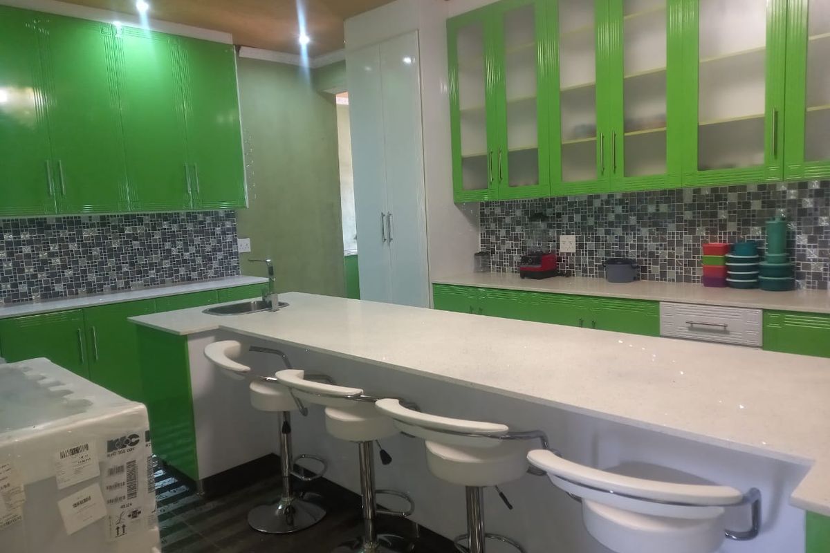 Modern kitchen featuring vibrant green cabinetry, a spacious quartz island with breakfast bar seating, and a decorative mosaic tile backsplash.