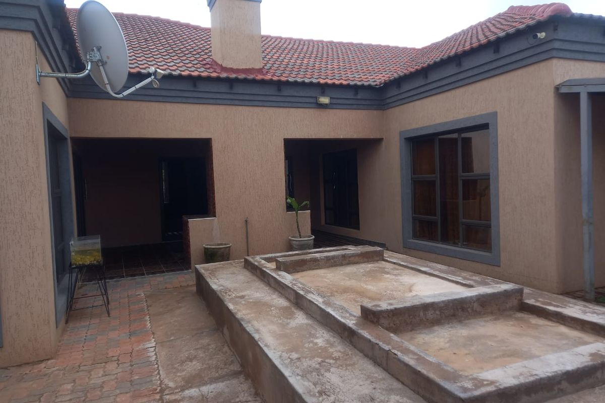 Rear exterior view of the house featuring a paved patio area with a raised concrete platform, terracotta roof tiles, and a chimney.
