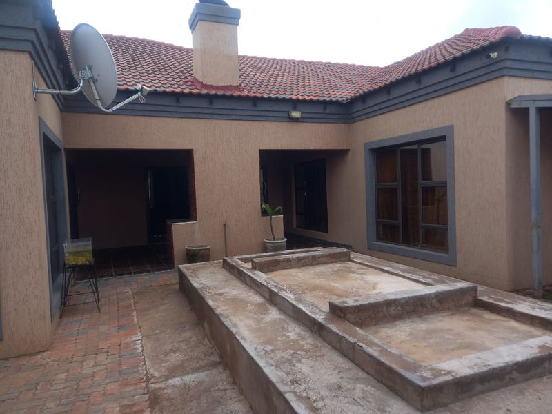 Rear exterior view of the house featuring a paved patio area with a raised concrete platform, terracotta roof tiles, and a chimney.