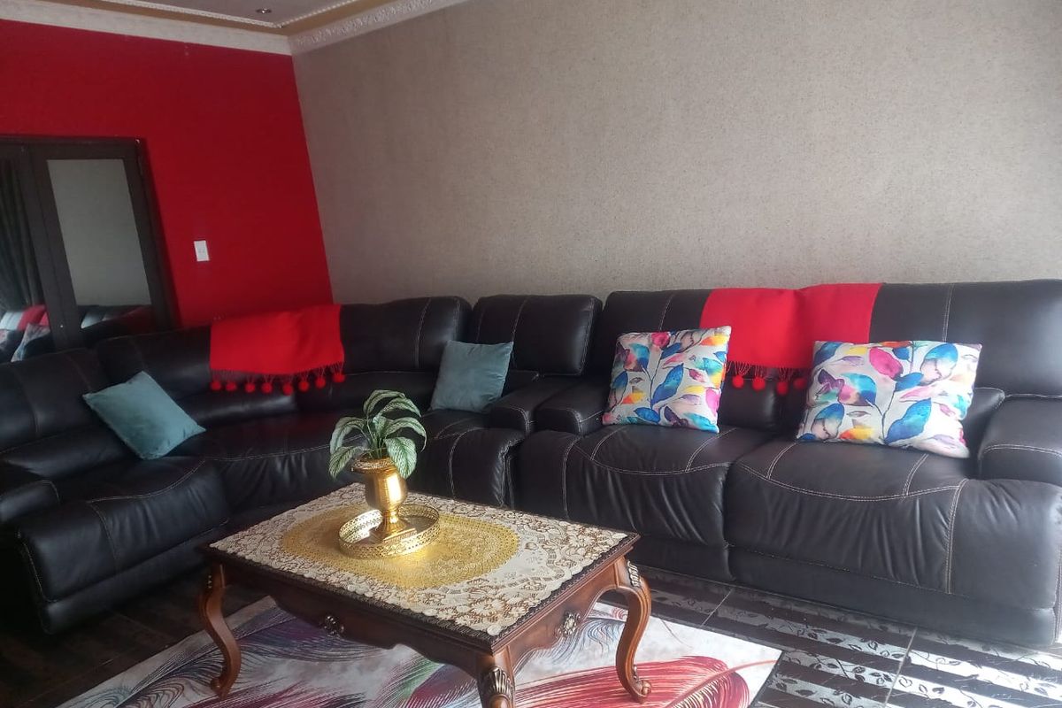 A living room featuring decorative ceiling cornices and tiled flooring, with a bold red accent wall.