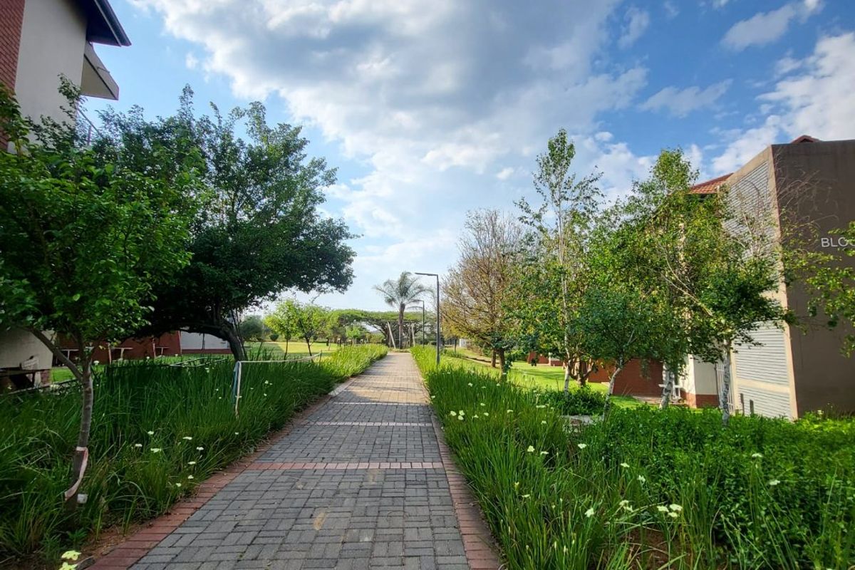 A well-maintained paved walkway leading through a landscaped garden area between apartment buildings.