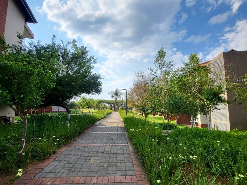 A well-maintained paved walkway leading through a landscaped garden area between apartment buildings.